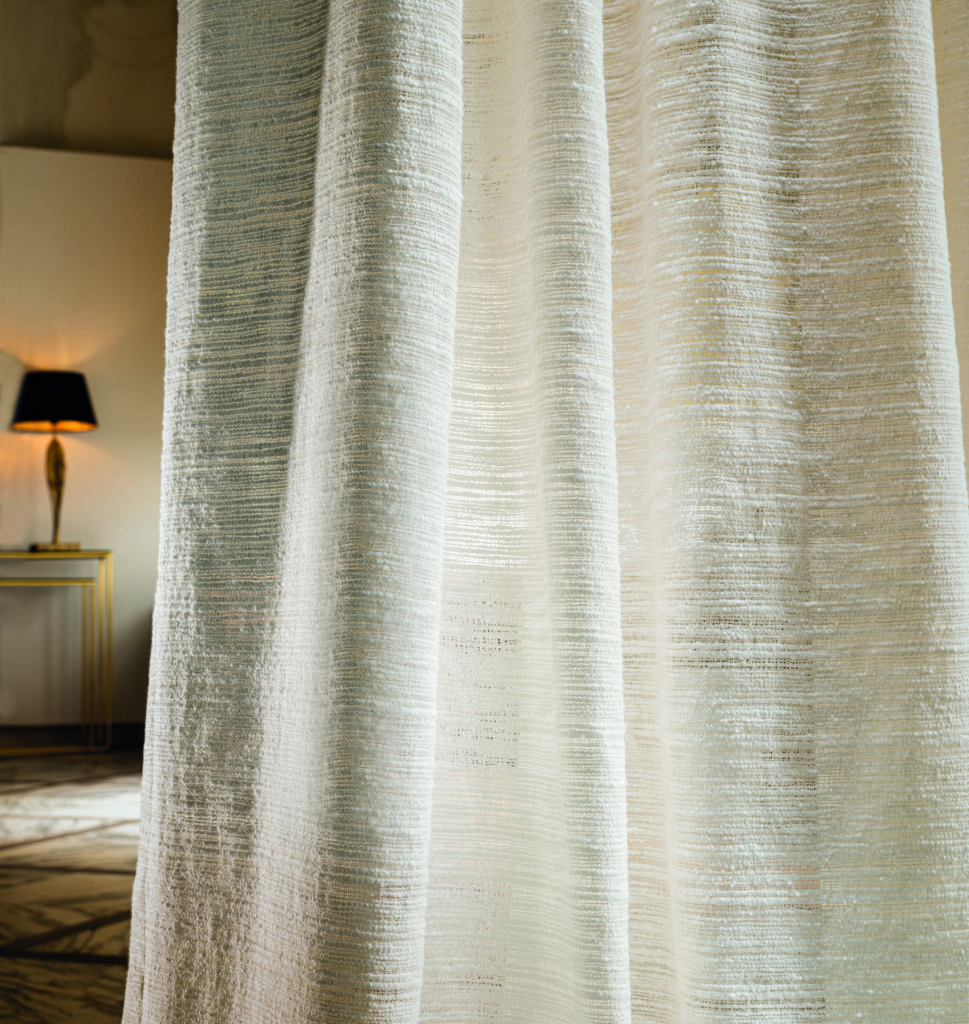 Created from an archive design, "Propolis" is a silk jacquard whose motif, close-up, recalls a beehive : the same twisted gold yarn seems to have been deposited in each of the eight-coloured cells. The silk satin warp adds brightness, creating matte and lustrous contrasts with the viscose and linen weft. The design repeats four times across the width. On a larger scale, we can perceive the scales of some fantastic animal who has decided to make their home on the azure-blue coast. This silk is ideal for making curtains, cushions and decorative seating. In eight very luxurious colours, Ivory, Bronze, Powder Pink, Arabesque, Celadon, Eternal Blue, Silver and Fuscous.